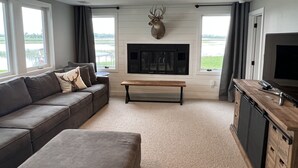 A modern living room with a grey sofa, a wooden coffee table, a mounted deer head, a fireplace, and a TV. - Perfect lake home for a family get away - Only 1 hour from metro (South Haven)