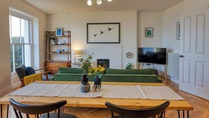 A living room with a green sofa, a wooden dining table, and a flat-screen TV. - The Lookout - Stylish penthouse with sea views (Ramsgate)