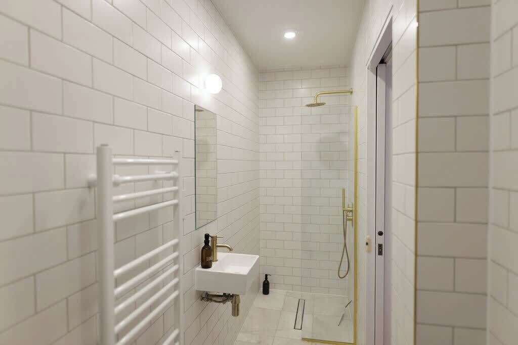 Un baño moderno con azulejos blancos, un lavamanos blanco, un espejo, un toallero y una zona de ducha.