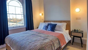 A bedroom with a large window, a bed with a patterned blanket, and a bedside table with a lamp. - The Lookout - Stylish penthouse with sea views (Ramsgate)
