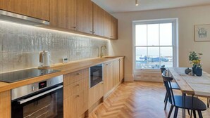 A modern kitchen with wooden cabinets, a built-in oven, and a large window offering a view. - The Lookout - Stylish penthouse with sea views (Ramsgate)