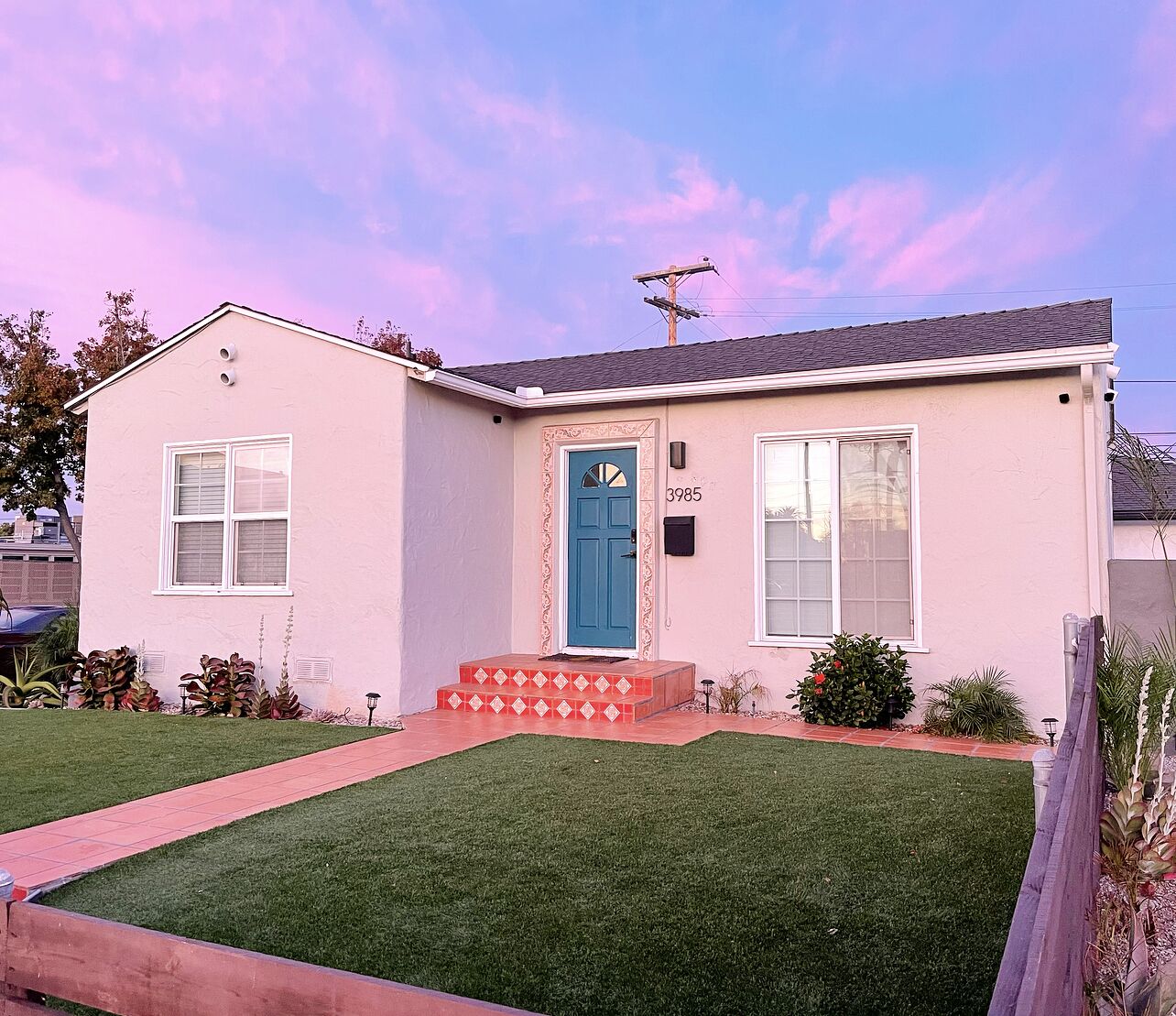 A single-story house with a blue front door, numbered 3985, and a small front yard with a red pathway.
