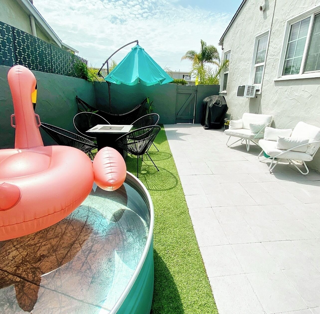 Un jardin avec une piscine, des jeux gonflables pour la piscine, un espace recouvert de gazon synthétique et des meubles d’extérieur.