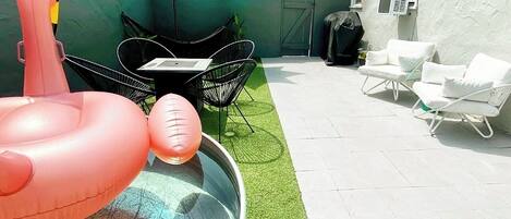 Un jardin avec une piscine, des jeux gonflables pour la piscine, un espace recouvert de gazon synthétique et des meubles d’extérieur.
