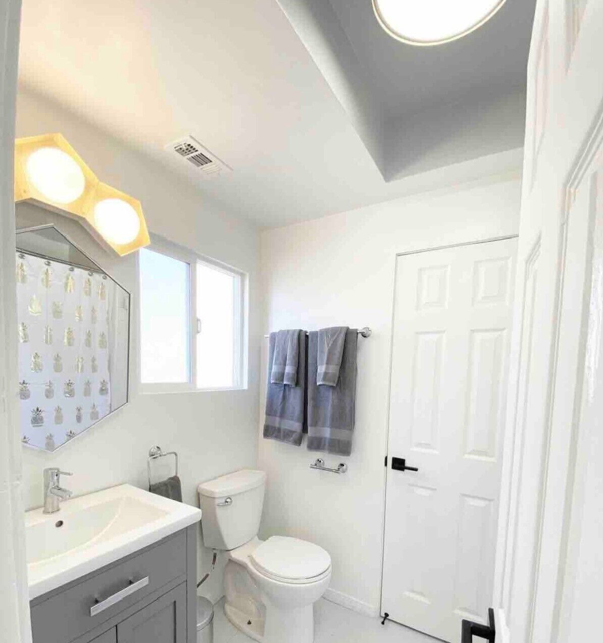 A bathroom with a white sink, mirror, and toilet. There is a window above the sink and a door to the right.