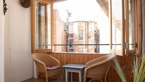 Ein Balkon mit Korbstühlen und einem kleinen Tisch, mit Blick auf ein Backsteingebäude.
