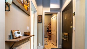 Un corridoio con pavimento in legno, un termosifone, un termostato, uno scaffale con una sveglia e una porta con inferriata.