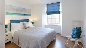 A bedroom with a bed, a nightstand, a chair, a window with a view, and a ceiling light. - A spacious open plan apartment, in an unbeatable city-centre location. Sleeps 4. (Edinburgh)