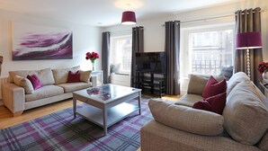 A modern living room with a sofa, a coffee table, and a flat-screen TV. - A spacious open plan apartment, in an unbeatable city-centre location. Sleeps 4. (Edinburgh)