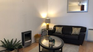 A living room with a black leather sofa, a glass coffee table, a fireplace, and a mirror on the wall. - Lovely one-bedroom apartment just a few yards off Edinburgh’s famous Royal Mile. Sleeps 2. (Edinburgh)