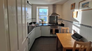 A compact kitchen with white cabinets, a black countertop, a window, and a wooden dining table. - Lovely one-bedroom apartment just a few yards off Edinburgh’s famous Royal Mile. Sleeps 2. (Edinburgh)