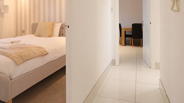 A hotel room with a bed, a bedside table, a chair, a small table with chairs, and a telephone.