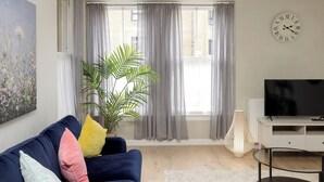 A modern living room with a sofa, a potted plant, a television, and a clock on the wall.