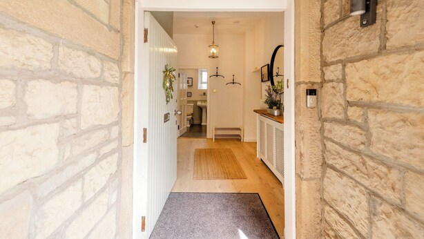 A hallway with a stone wall, a wooden floor, a door, a bench, and a hanging light fixture.