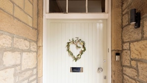 A white door with a heart-shaped wreath, a small plaque, and a doorbell.