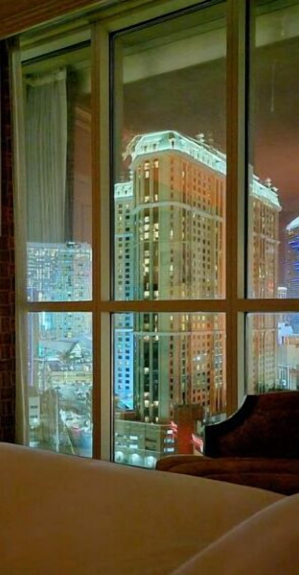 Una camera d'albergo con una grande finestra che si affaccia su un alto edificio con molti piani e luci.