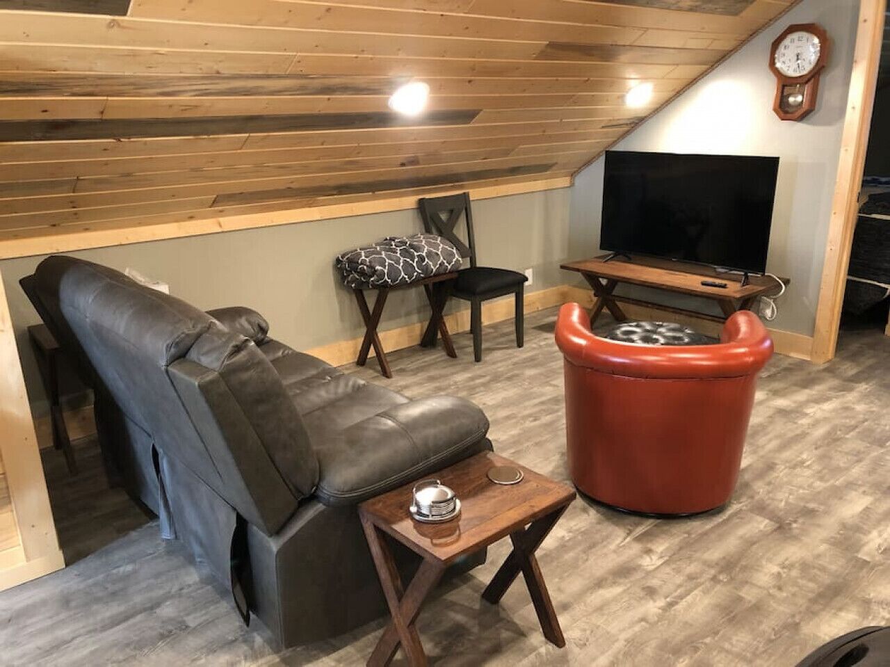 Un salon chaleureux avec un canapé en cuir, une petite table agrémentée d’un objet décoratif, une poubelle rouge et un téléviseur.