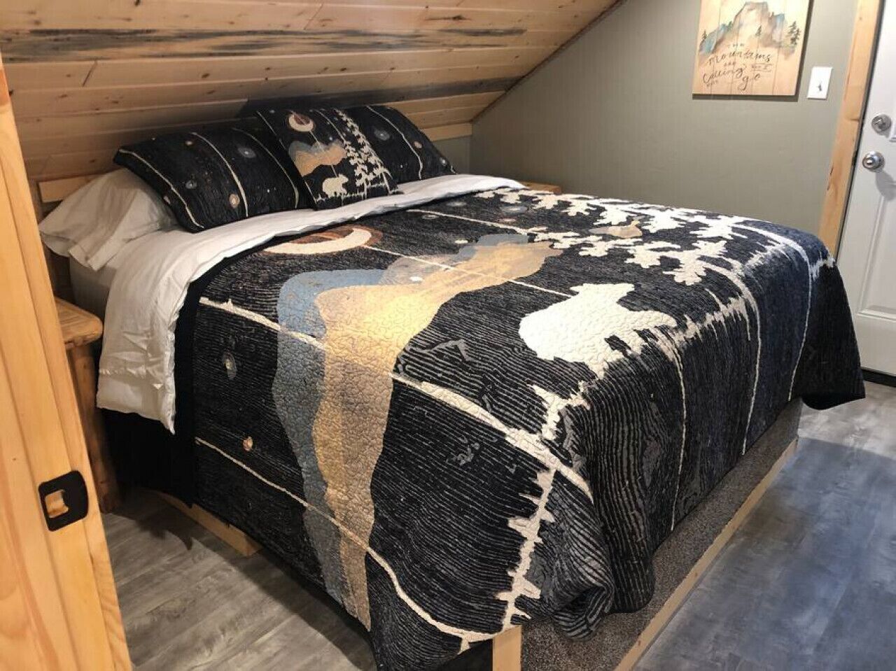 Une chambre à coucher avec un lit recouvert d’une couverture à motifs, une tête de lit en bois et une porte ornée d’un tableau.