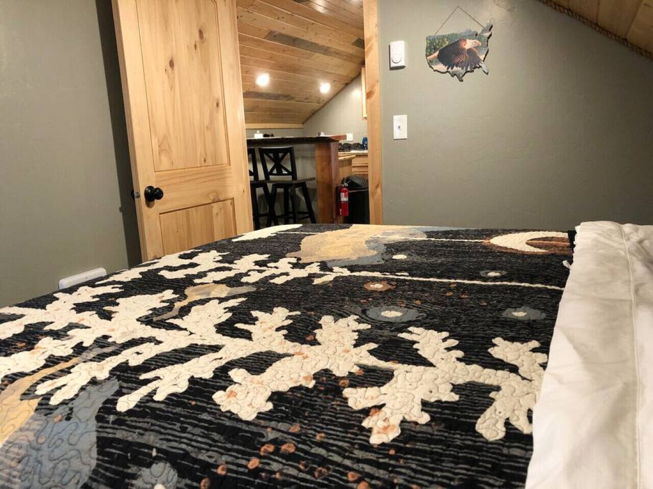 Une pièce avec un tapis à motifs, une porte en bois, une petite table avec des chaises et un élément décoratif fixé au mur.
