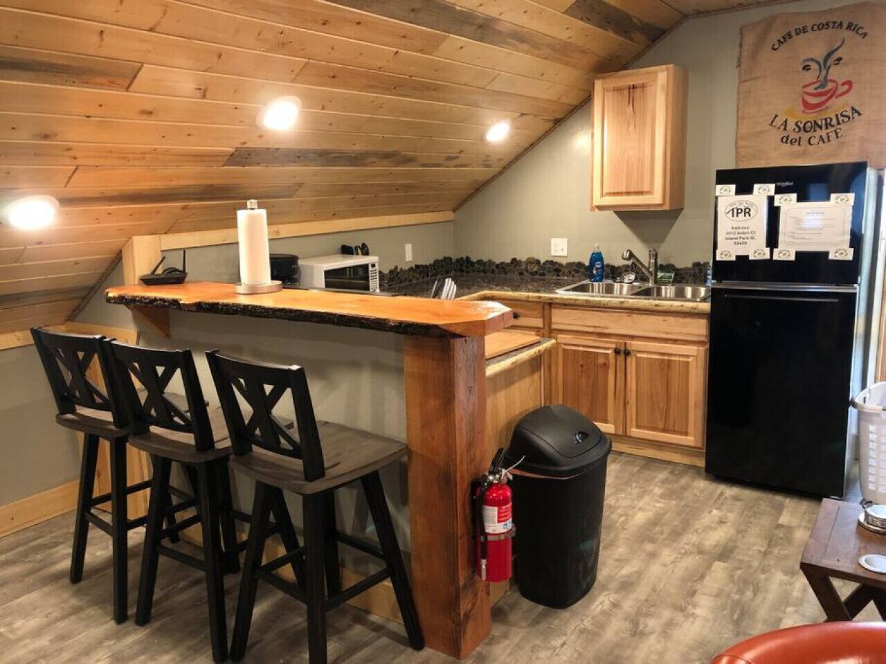 Eine Küche mit Holzausbau, einem schwarzen Kühlschrank, einer Holzbar und zwei Barhocker.
