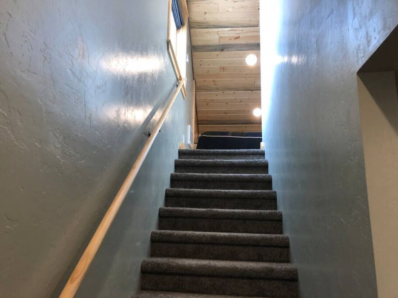 A carpeted staircase with wooden handrails and a wooden ceiling.
