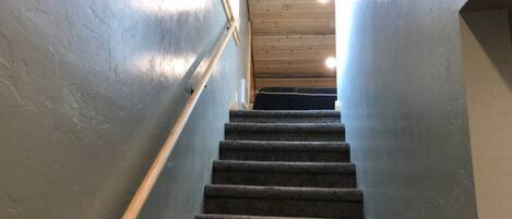 A carpeted staircase with wooden handrails and a wooden ceiling.