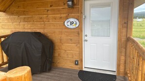 Eine Holzhütte mit weißer Tür, einer überdachten Grillstelle und einer kleinen Sitzgruppe im Freien.