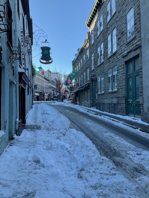 A snow-covered street with historic buildings, a pub sign, and flags. - Historic District of Old Quebec. 1-bedroom apartment, sleeps 4 (Québec)