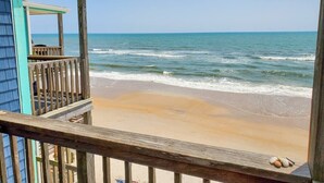 A beach view with a wooden deck and a building with a blue exterior. - The Lookout: Tranquil Beachfront Condo (North Topsail Beach)