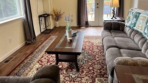 A living room with a sofa, a coffee table, a TV, and a door leading to an outdoor area.