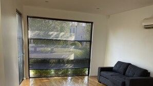 Una sala de estar moderna con piso de madera, un sofá oscuro y un ventanal con persianas.