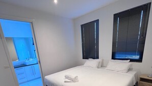 Una habitación de hotel moderna con una cama grande, una mesita de noche y una ventana con persianas.
