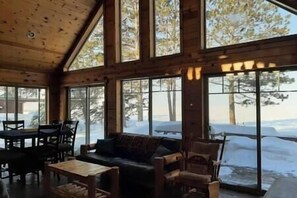 A log cabin interior with a large window overlooking a snowy landscape.