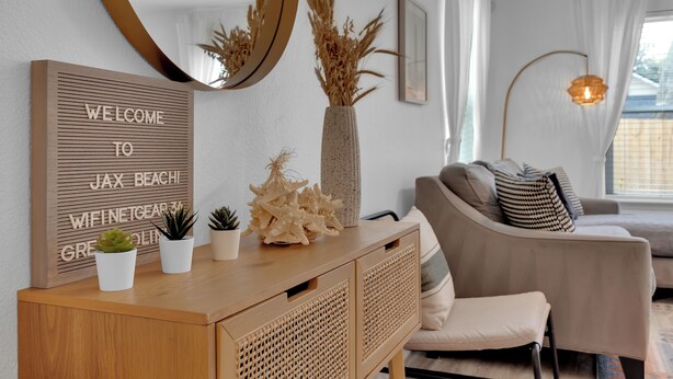 Een moderne woonkamer met een houten console, een welkomstbord, een grote spiegel, een bank en een decoratieve vaas.