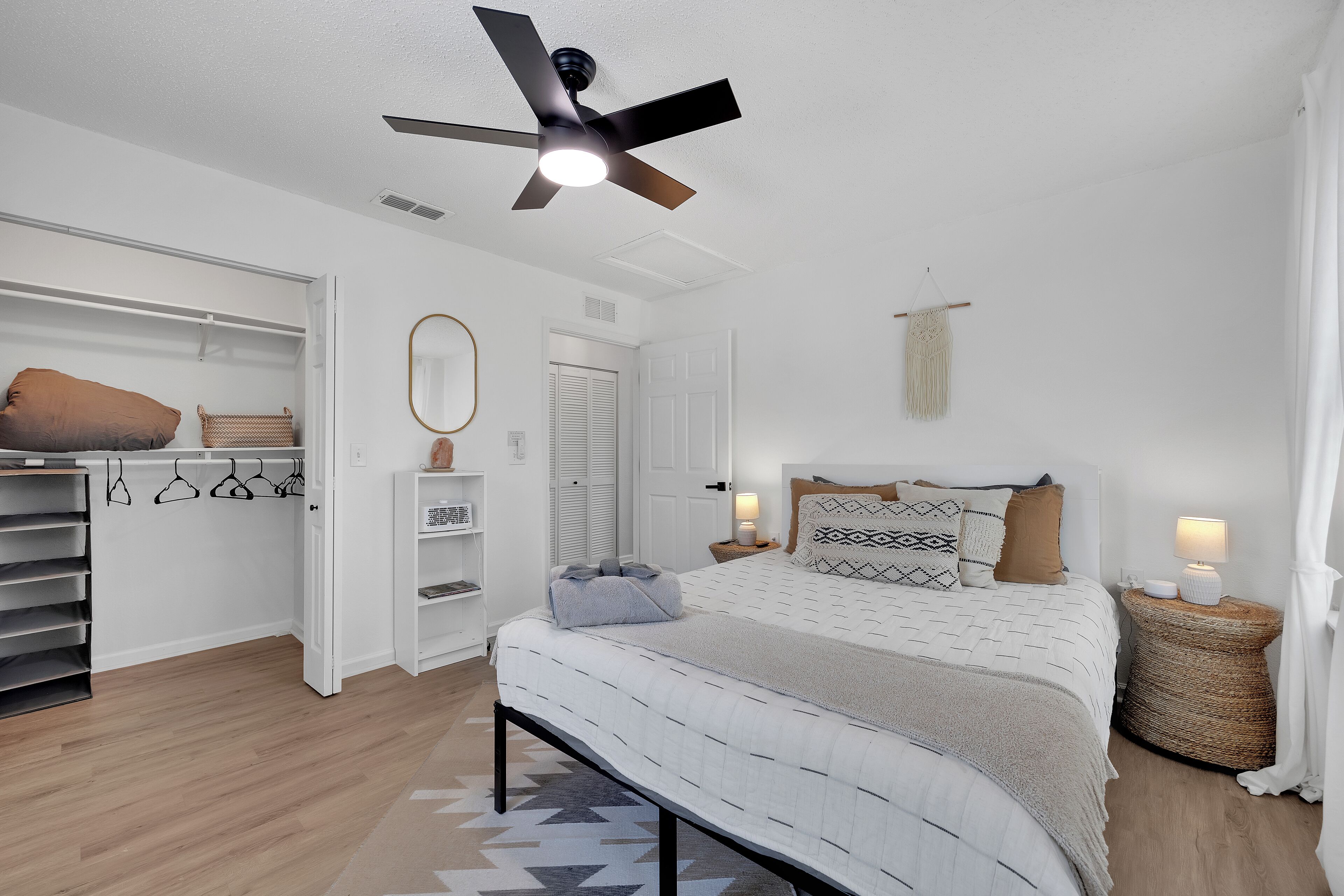Un dormitorio con cama, mesitas de noche, ventilador de techo, armario y perchero.