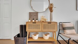 Een kamer met een houten console tafel, een spiegel, een bord met een welkomstboodschap, een stoel en een mand.
