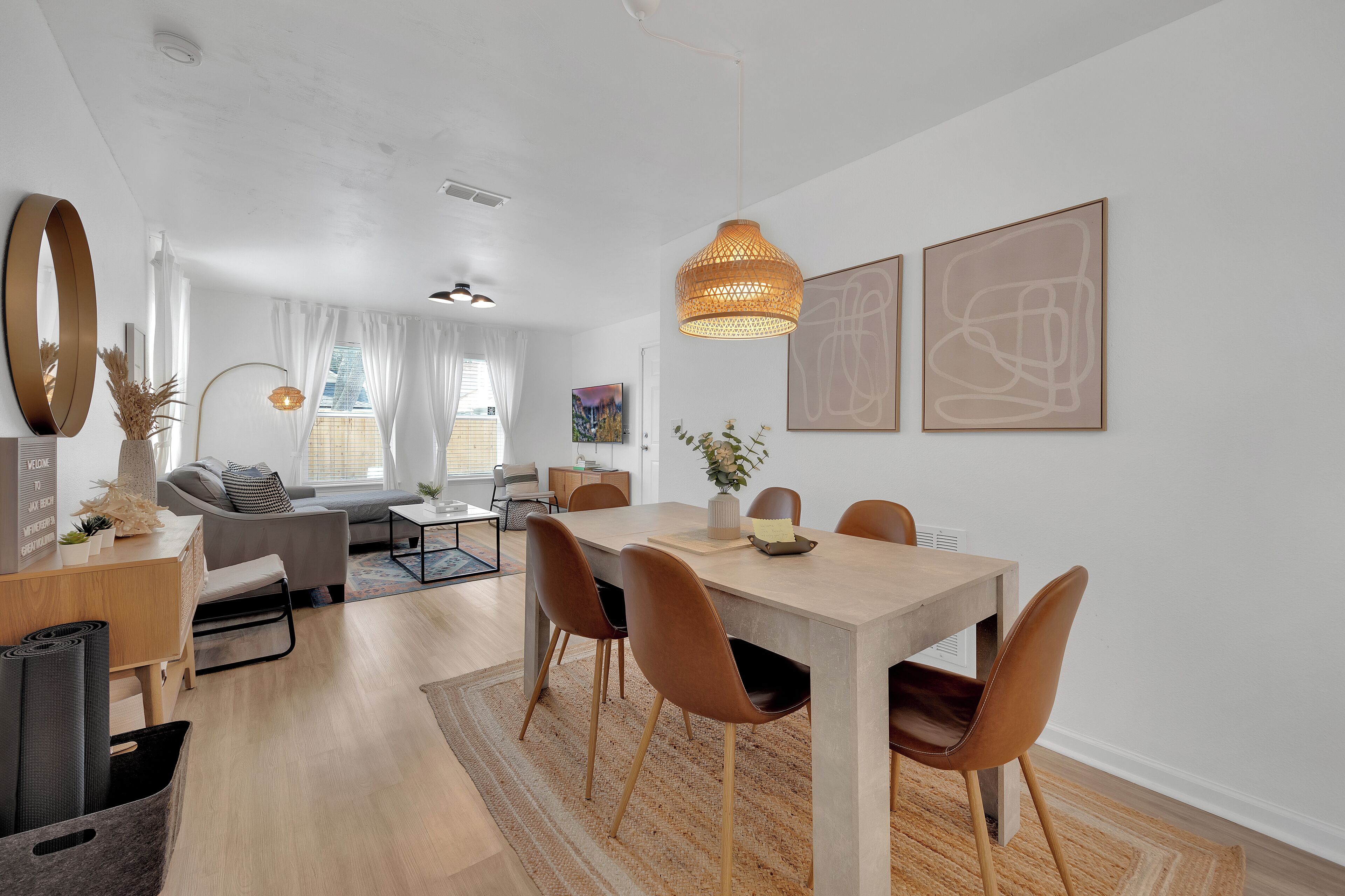 A modern living room with a dining area, featuring a wooden dining table, brown chairs, a large mirror, and artwork on the walls.