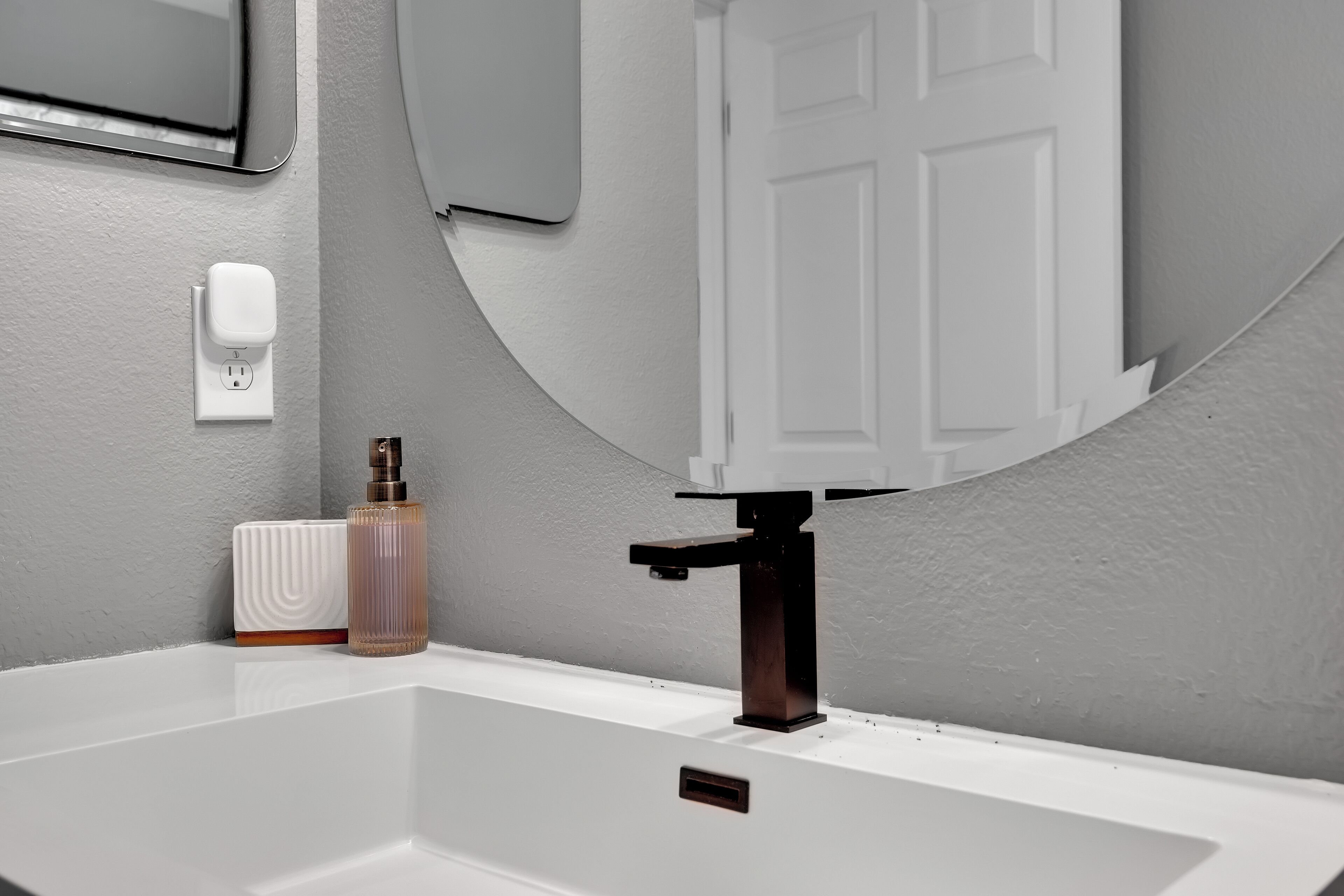 A bathroom with a white sink, a mirror, and a soap dispenser on the wall.
