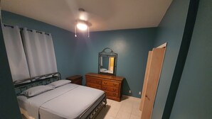 Quarto com cama, cômoda, espelho e porta.