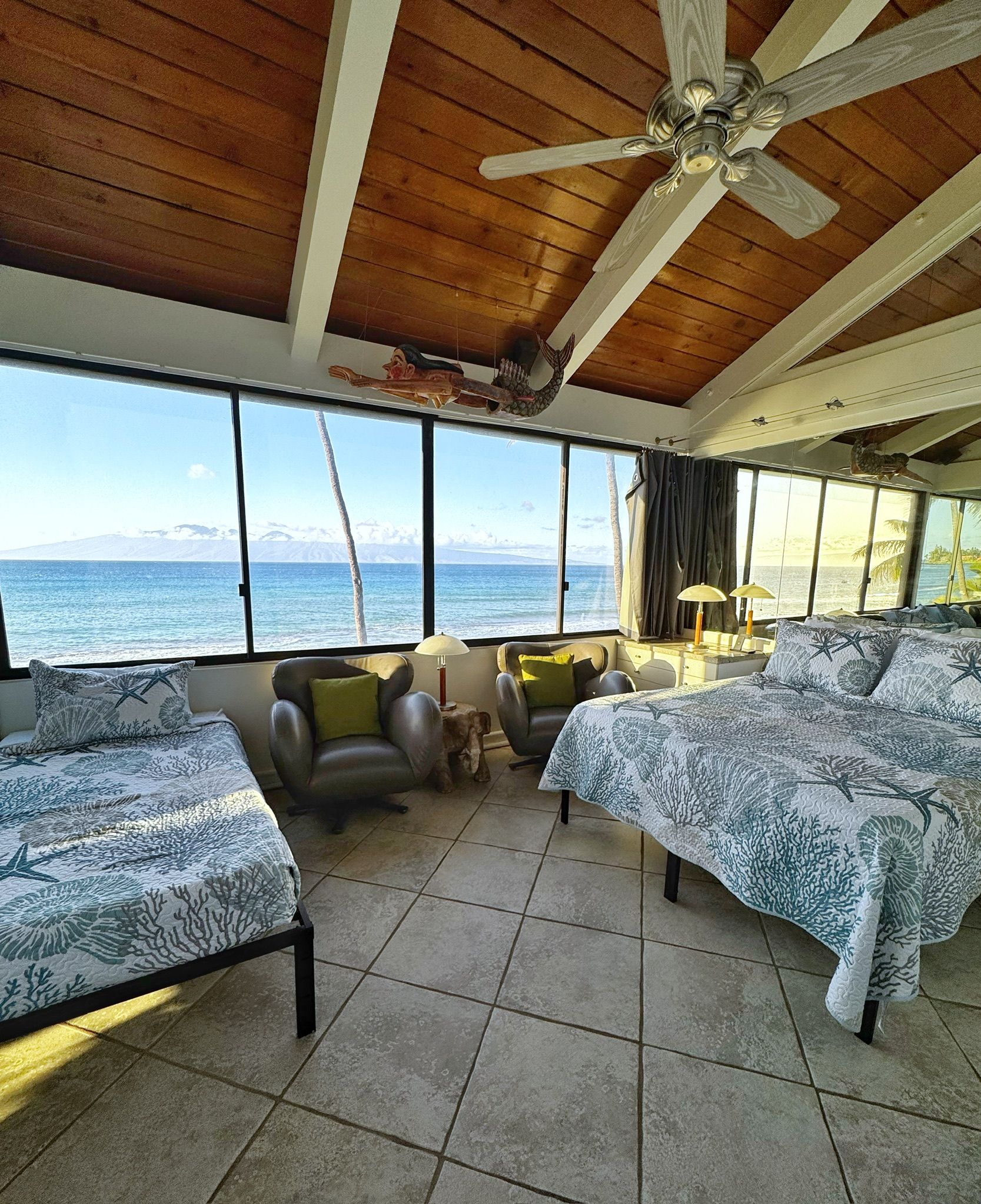 A room with two beds, a ceiling fan, and a view of the ocean.