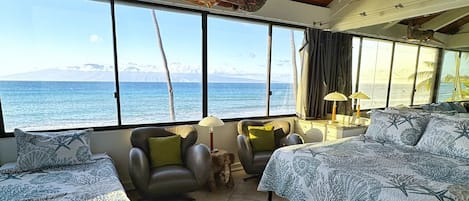 A room with two beds, a ceiling fan, and a view of the ocean.