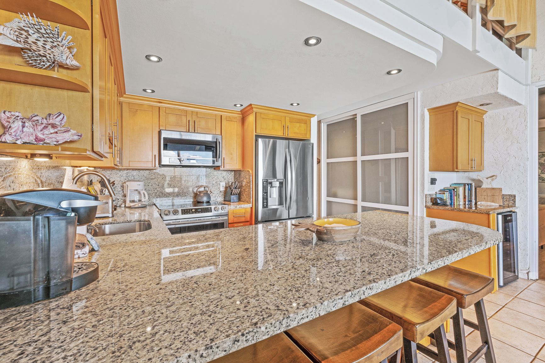 A kitchen with granite countertops, stainless steel appliances, wooden cabinets, and a large window.