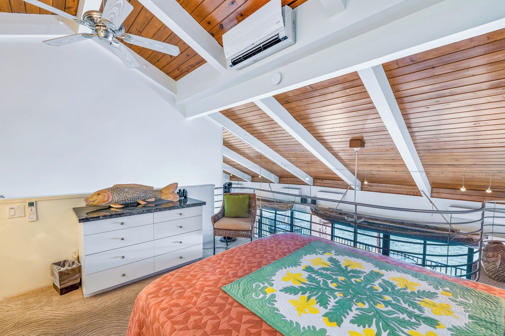 Un dormitorio con cama, cómoda, ventilador de techo y vista al mar a través de amplios ventanales.