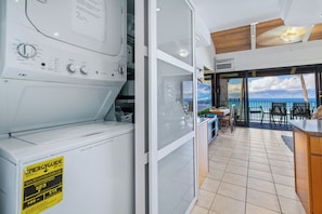 A modern kitchen with a built-in washer and dryer, a balcony with outdoor seating, and a view of the sea.