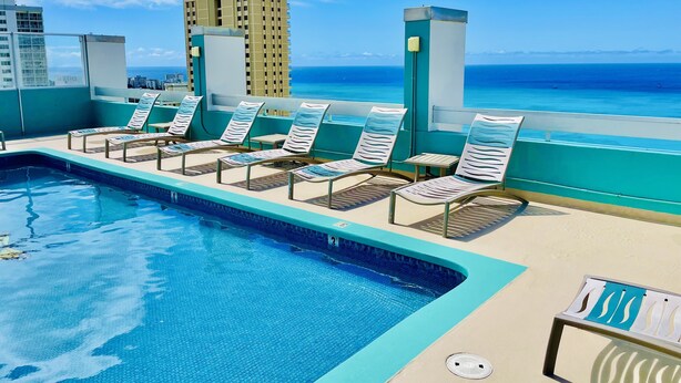 A rooftop pool area with lounge chairs and a view of the ocean.