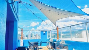 A rooftop patio with outdoor seating, a grill, and a view of the city skyline.