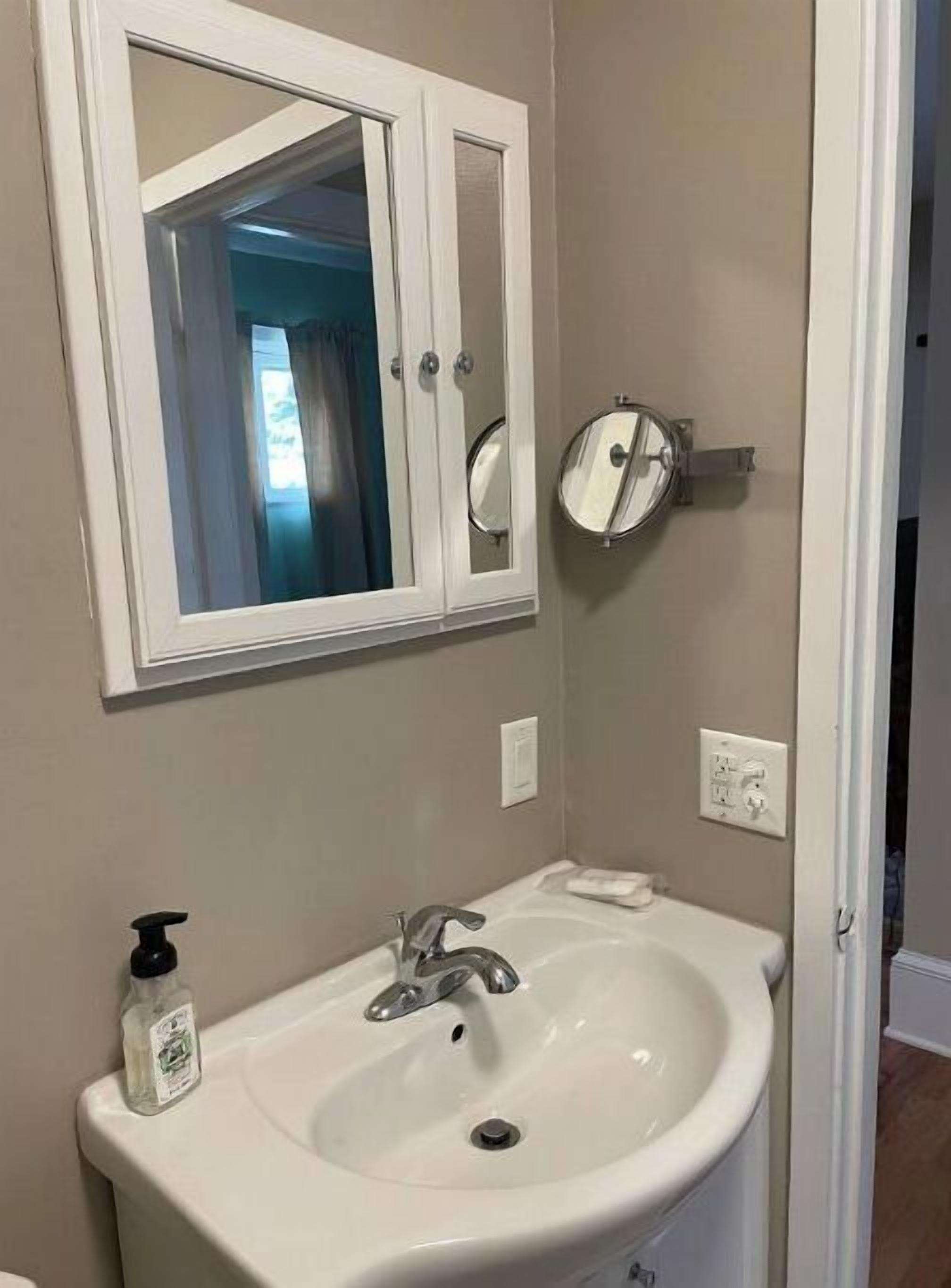 A bathroom with a white sink, a mirror cabinet, and a handheld mirror.