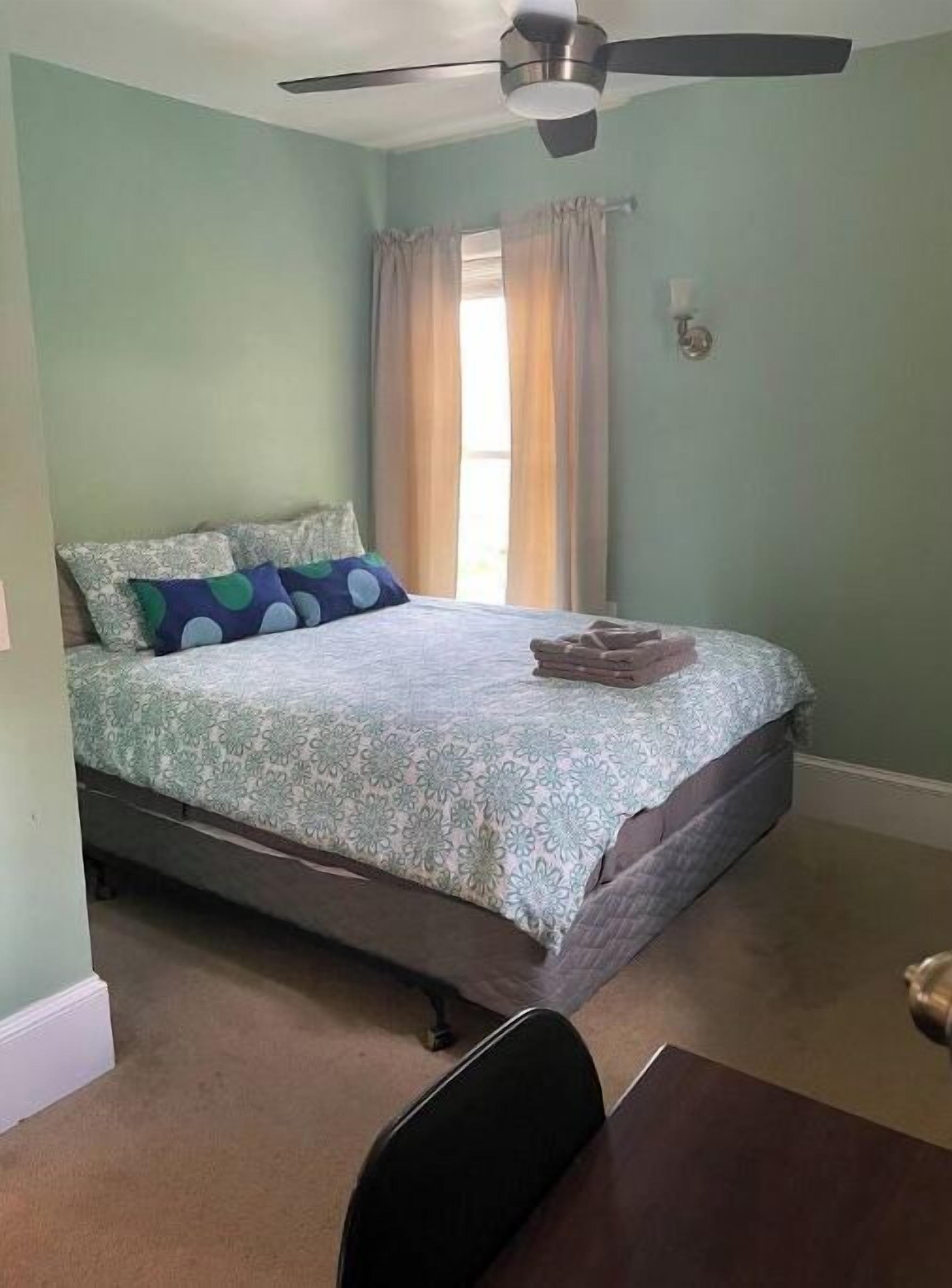 Un dormitorio con una cama, un ventilador de techo y una ventana con cortinas.