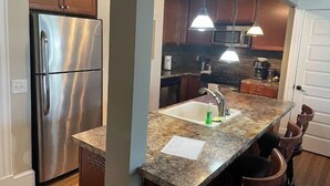 Una cocina moderna con refrigerador de acero inoxidable, encimeras de granito, un lavamanos con grifo e iluminación colgante.