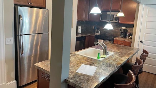 Una cocina moderna con refrigerador de acero inoxidable, encimeras de granito, un lavamanos con grifo e iluminación colgante.